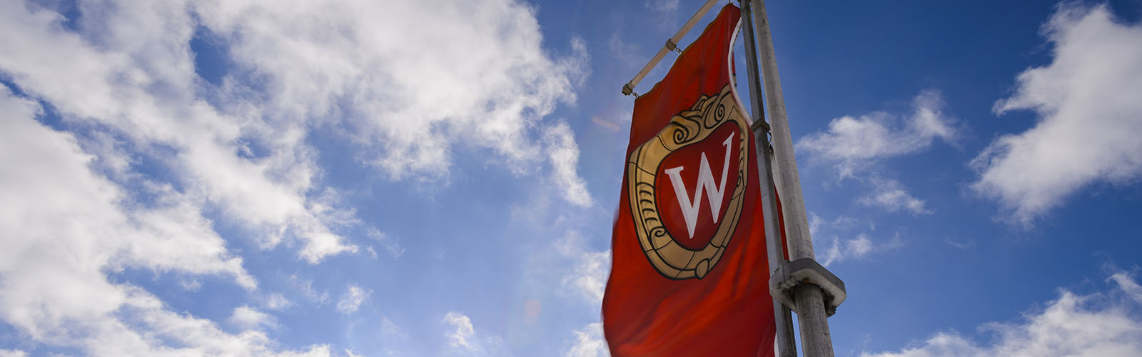 A UW flag against a blue sky with puffy clouds